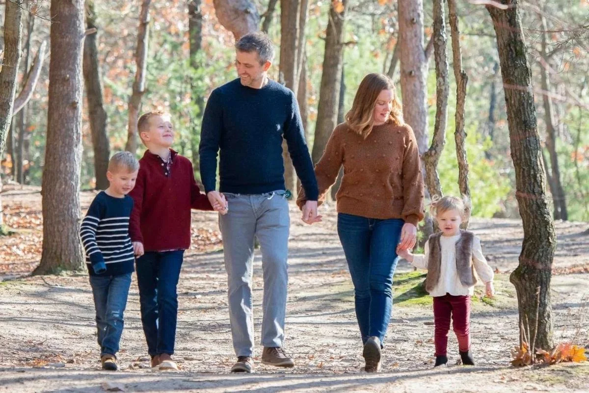 Bordoli family of five walking hand-in-hand along a wooded path in matching earth-toned outfits