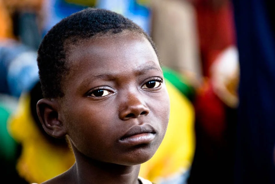 Close-up of a young girl with short curly hair and serious expression, in a colorful background.