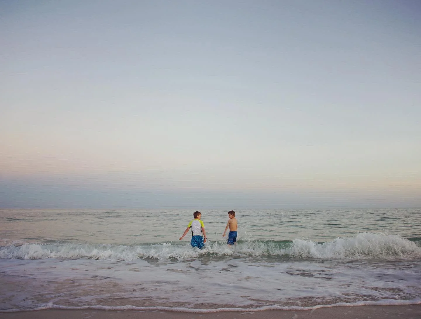 Two children playing in the ocean waves at the beach during sunset.