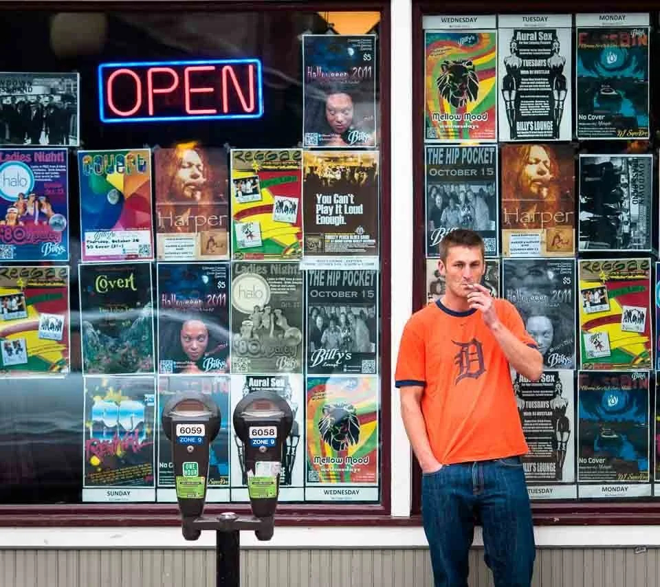 [10/100] Jeremy - As I passed, Jeremy stepped out of a local bar to take a smoke break while watching the Tigers game. The vibrance of the orange shirt and of the band flyers jumped out at me. Jeremy's a nice guy and had no problem at all with the sh