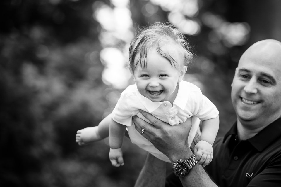 A man holding a smiling young child outside in a natural setting.