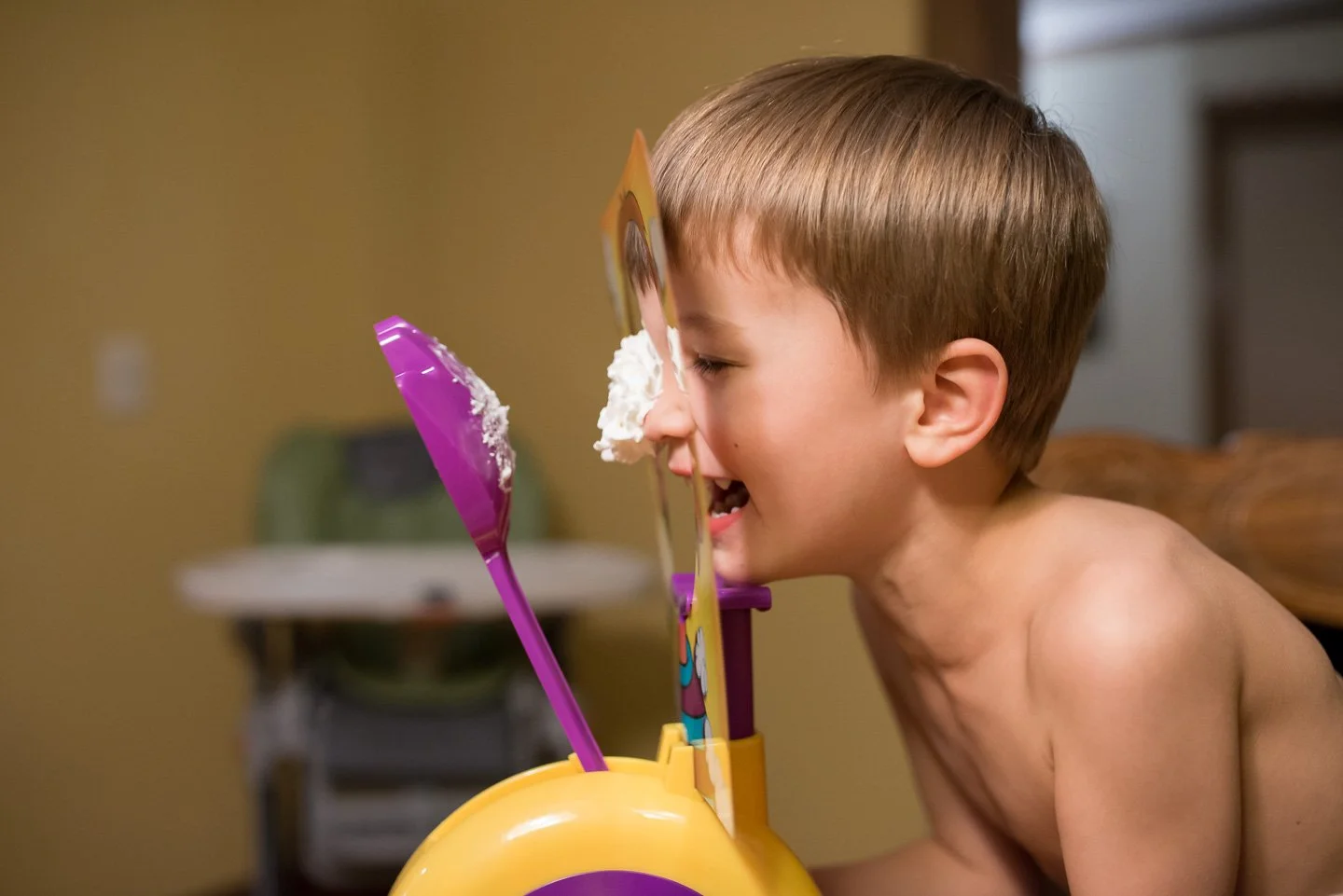 A young shirtless boy playing with a toy cake with whipped cream and plastic utensils.