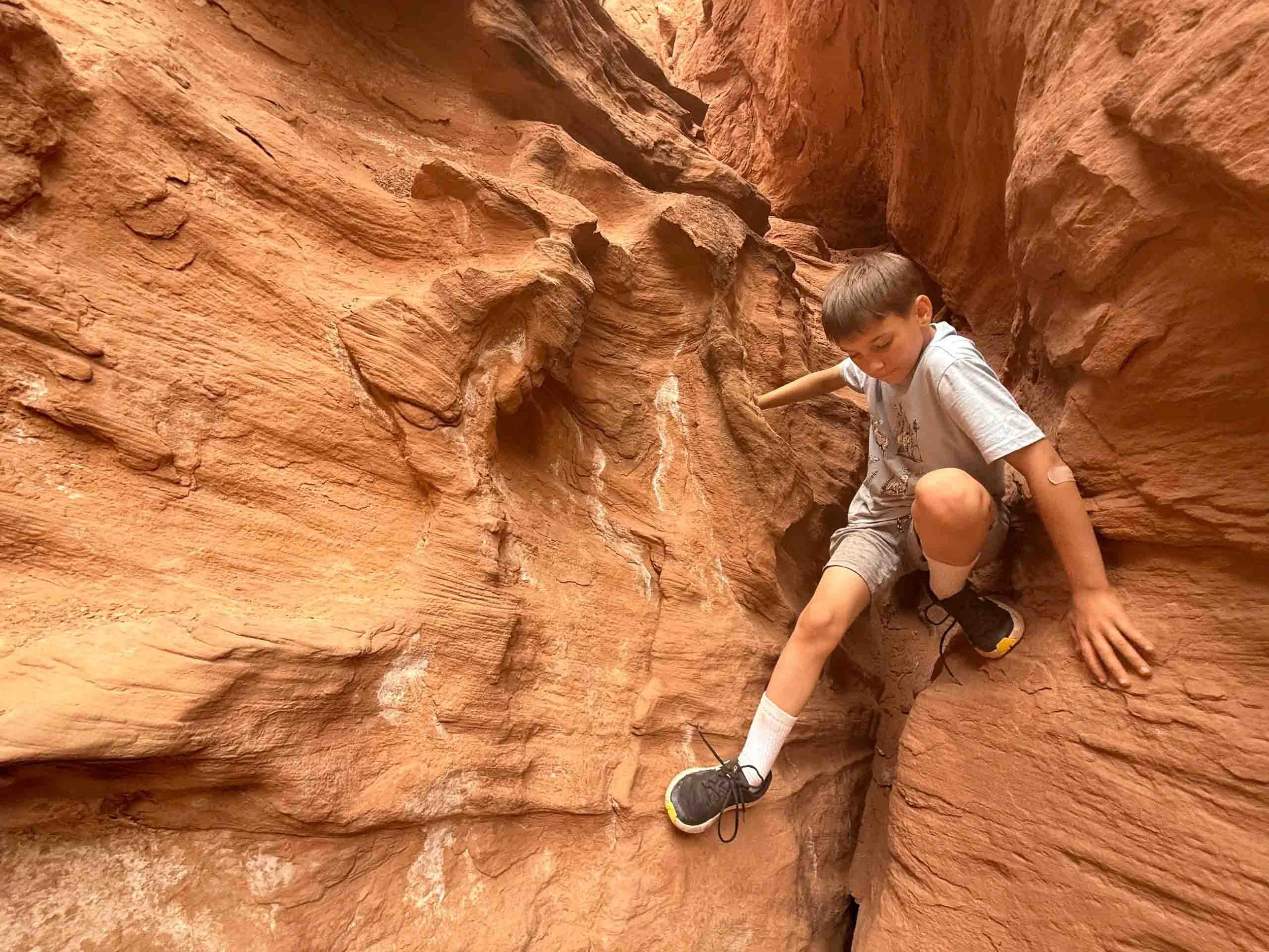 A young boy rock climbing in a narrow red sandstone canyon.
