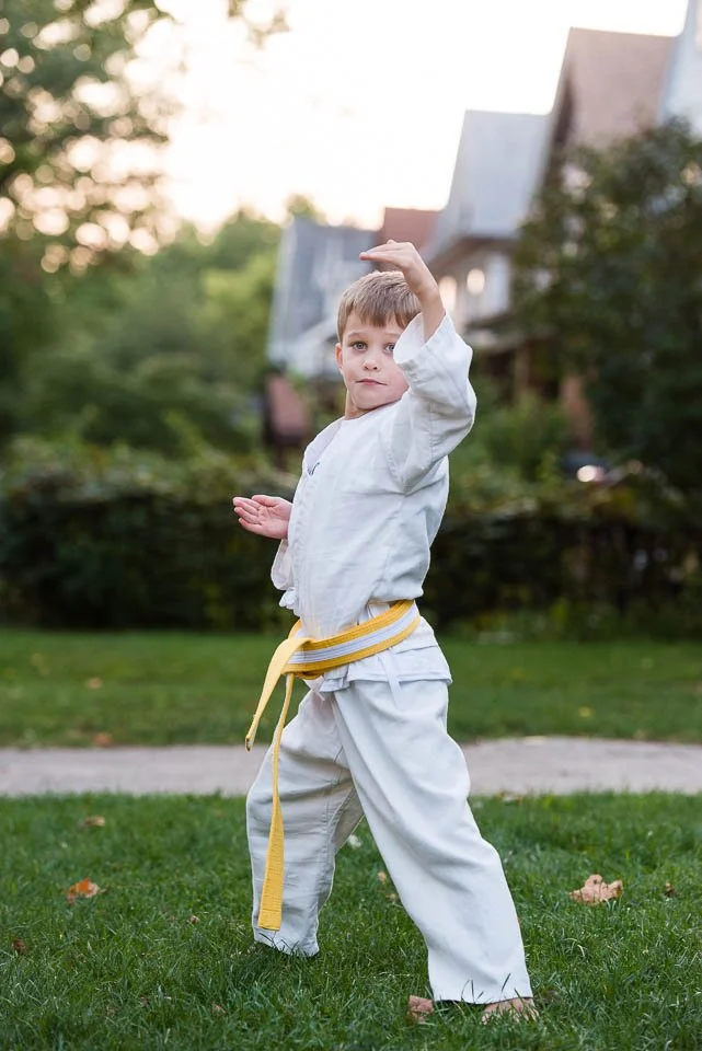 Young boy practicing martial arts outdoors on grass, wearing a white gi and a yellow belt, with a determined expression.