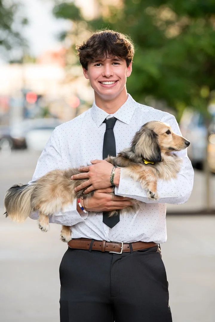 Senior portrait in a dress shirt and tie holding the family's dachshund on a downtown Grand Rapids street