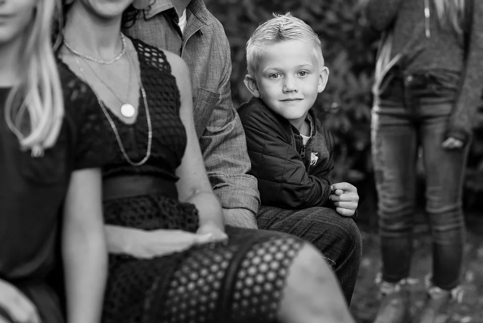 A group of people sitting outdoors, with a young boy in focus, looking at the camera in a black-and-white photo.