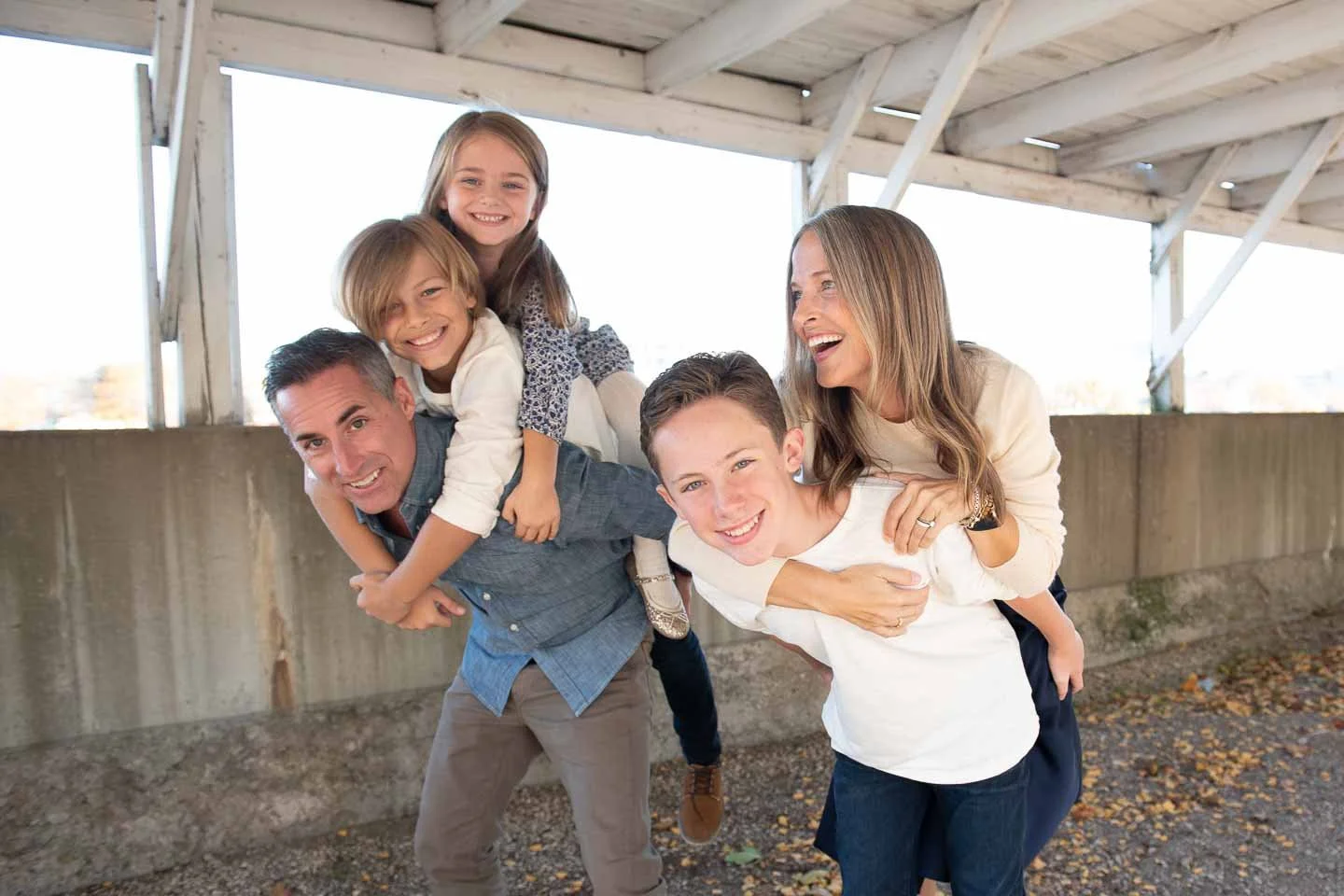 A family enjoying their time together outdoors, with two adults (a man and a woman) and three children, all smiling and having fun under a wooden structure.
