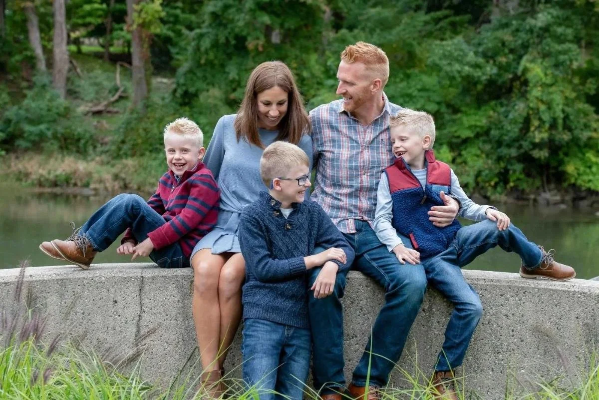 Family posing together on a stone wall along the Grand River in coordinated fall outfits