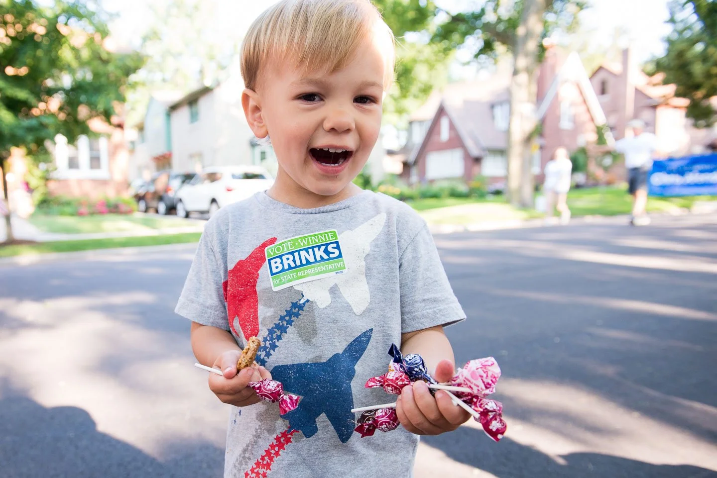 Young boy holding lollipops and cookie on a stick outdoors in neighborhood