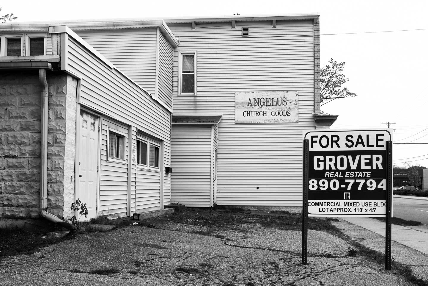 A black and white photo of a building with a sign that reads 'Angelus Church Goods' and a large 'For Sale' sign in front that provides contact information and details for a commercial property.