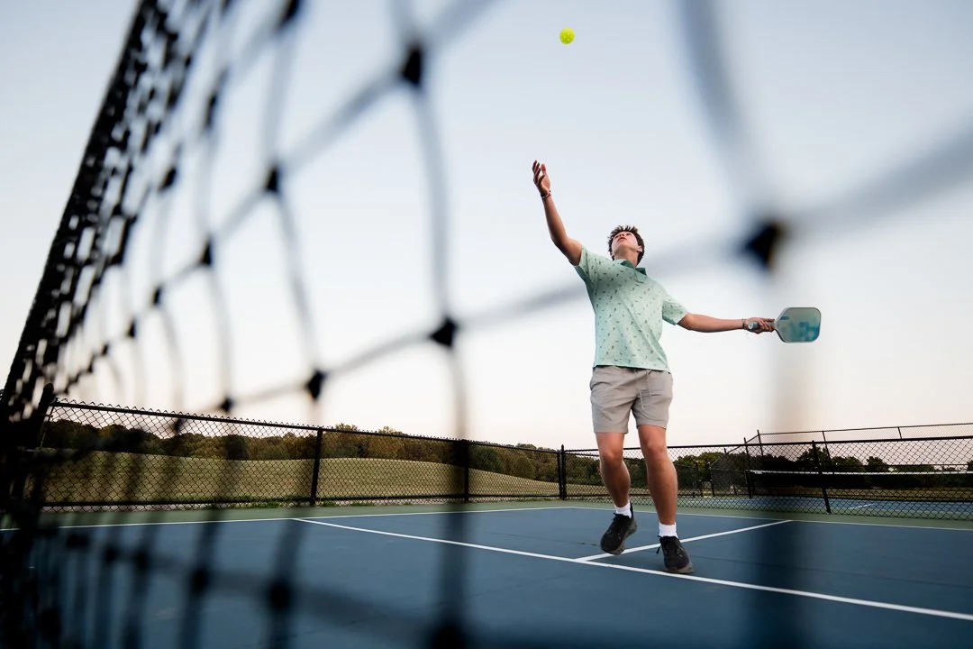Senior serving a pickleball at golden hour, shot through the net