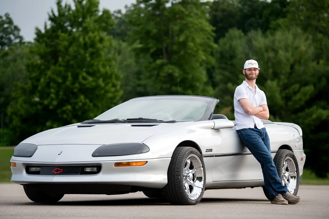 Senior portrait leaning against a white Chevrolet Camaro Z28 convertible