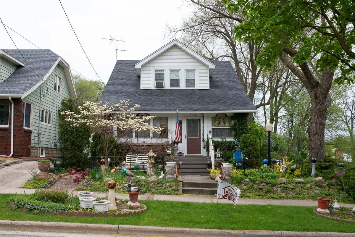 Front yard of a house with lawn, garden decorations, trees, and a sidewalk