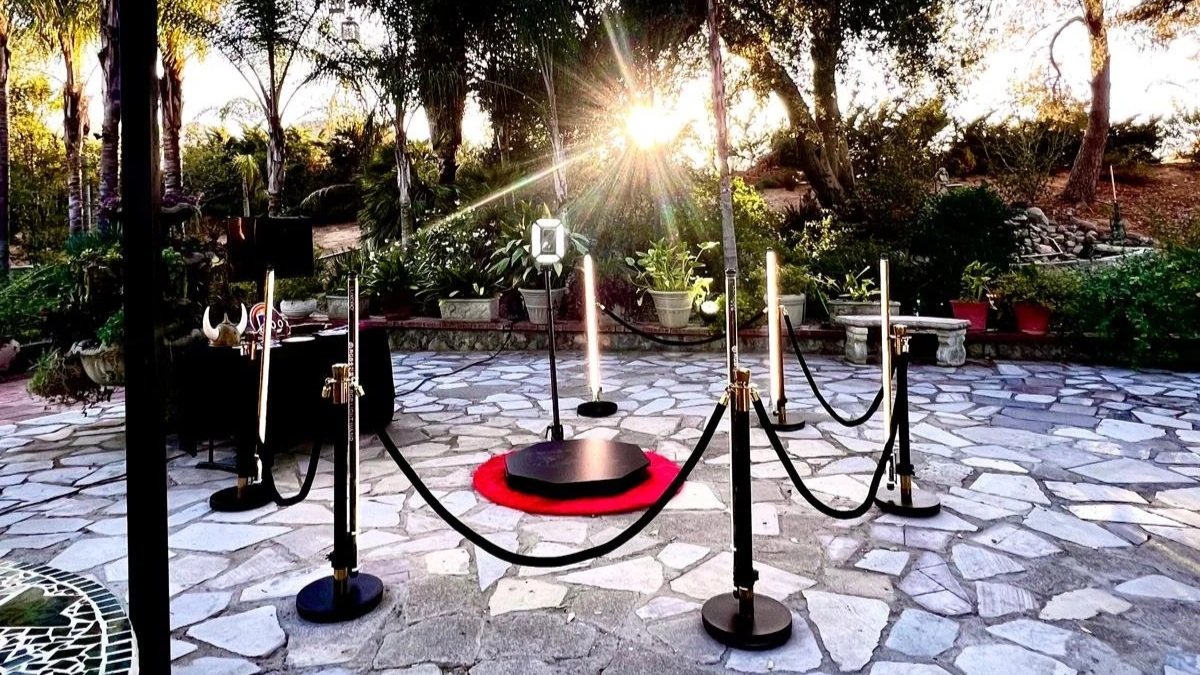 A small stage with a red carpet, candles, and spotlights outdoors during sunset, surrounded by a black rope barrier.