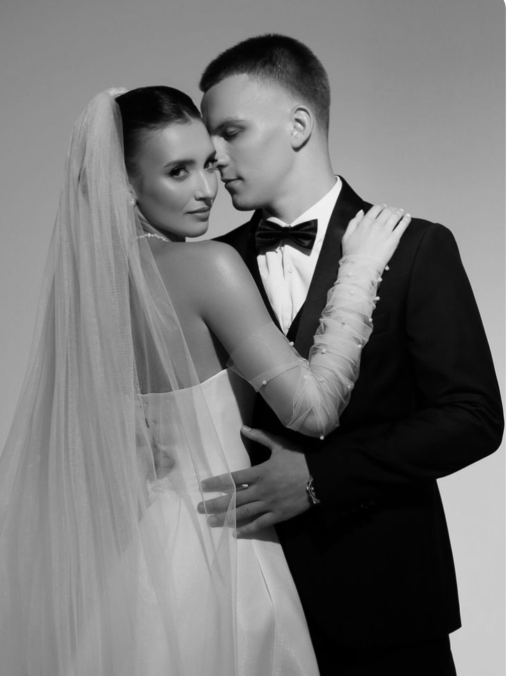 Black and white photo of a bride and groom in wedding attire, embracing and looking at the camera