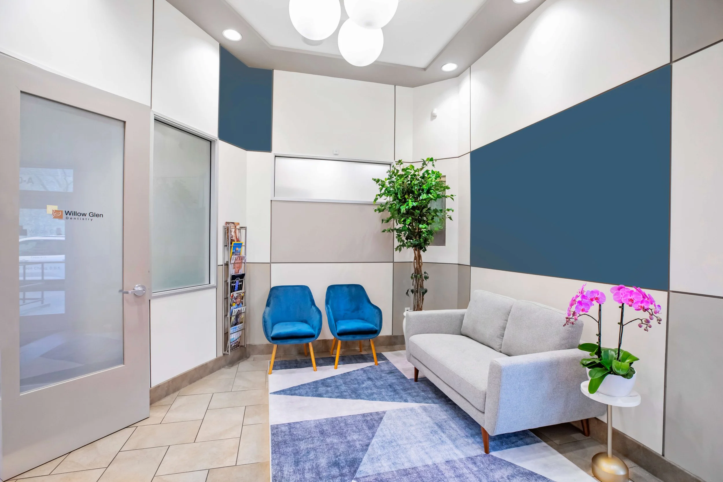 A modern and clean reception area with a gray couch, two blue chairs, a potted plant, bright lighting, and decorative wall panels at Willow Glen Dentistry.