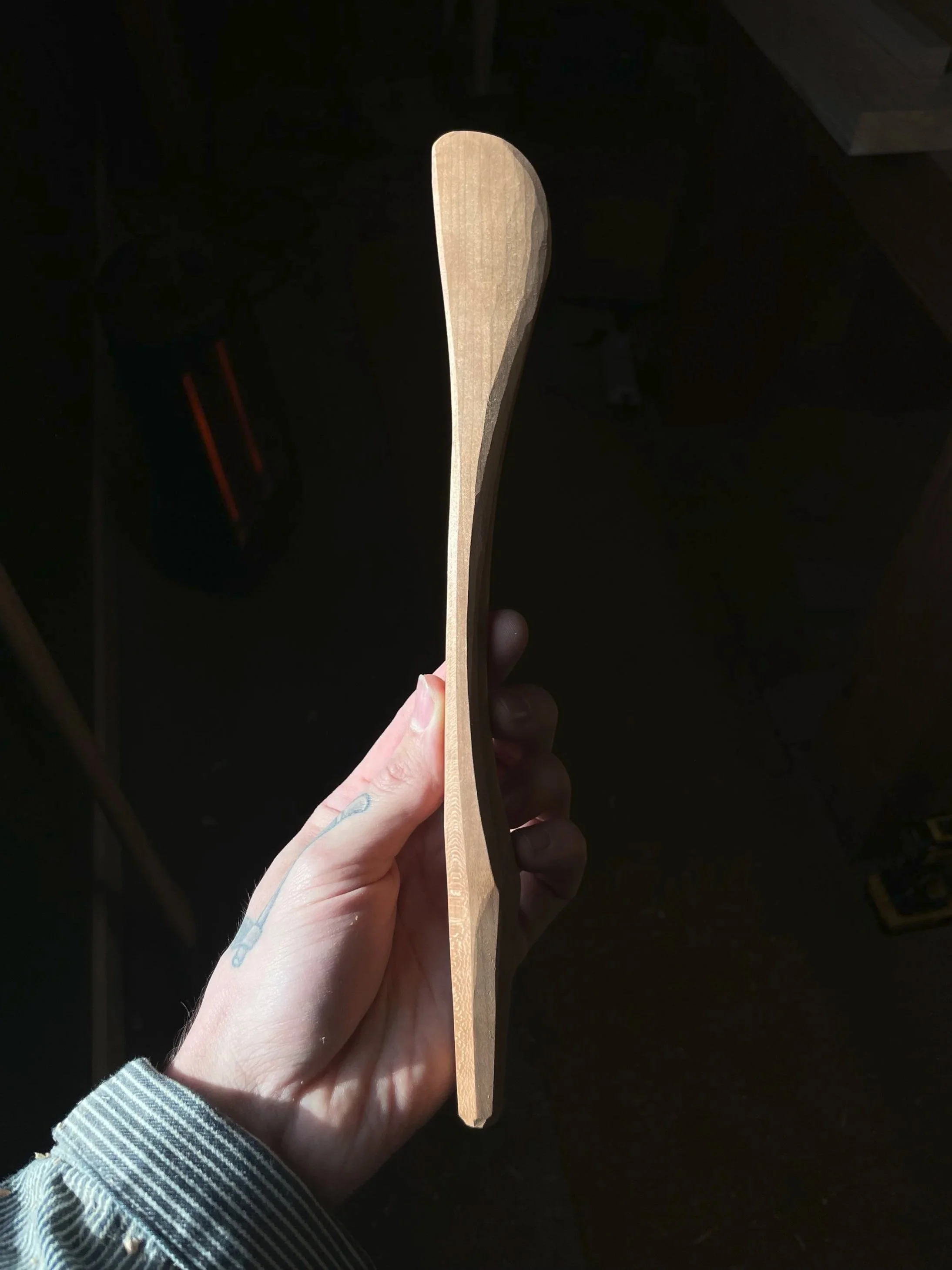 A hand holding a curved wooden spatula with carved facets and a smooth finish.