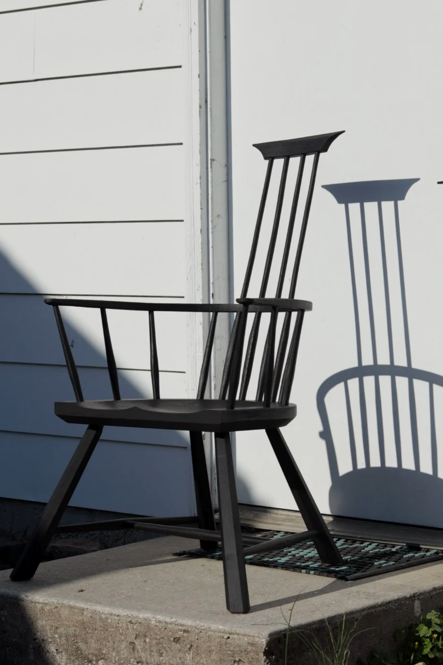 Black wooden chair casting a shadow on a white wall outside, next to a gray concrete step.