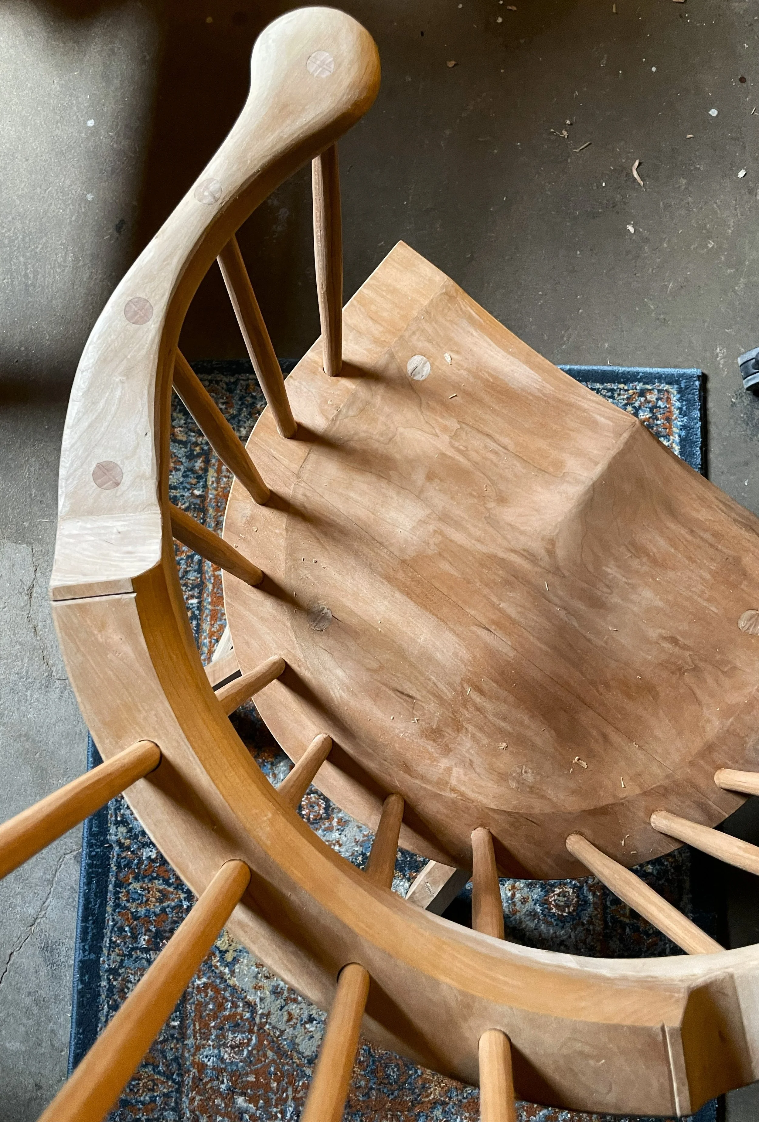 Overhead view of a wooden chair on top of a patterned rug, showing the seat, armrest, and vertical spindles on the backrest.