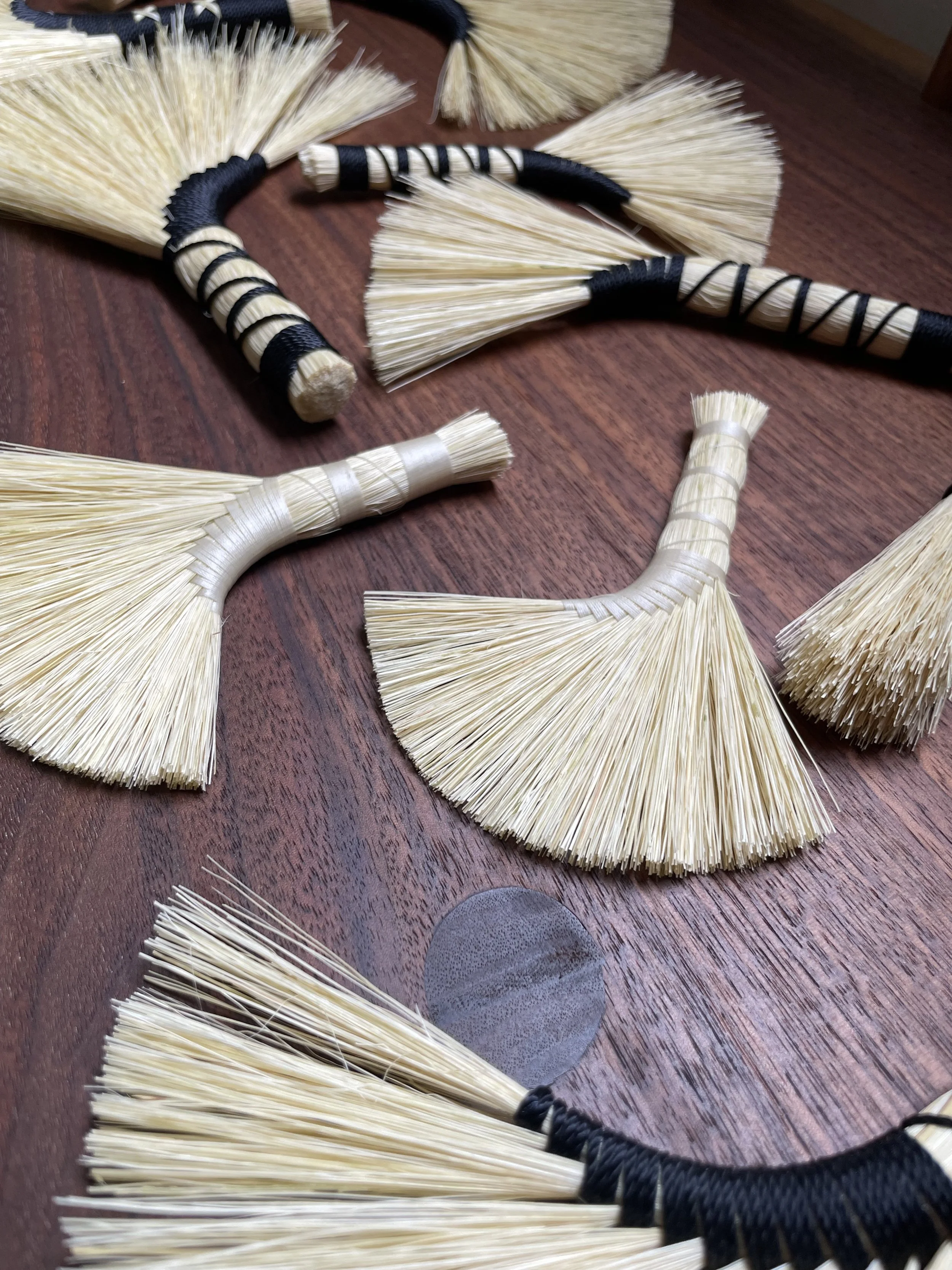 Several small handcrafted brooms with straw bristles and black or white wrapped handles on a wooden surface.