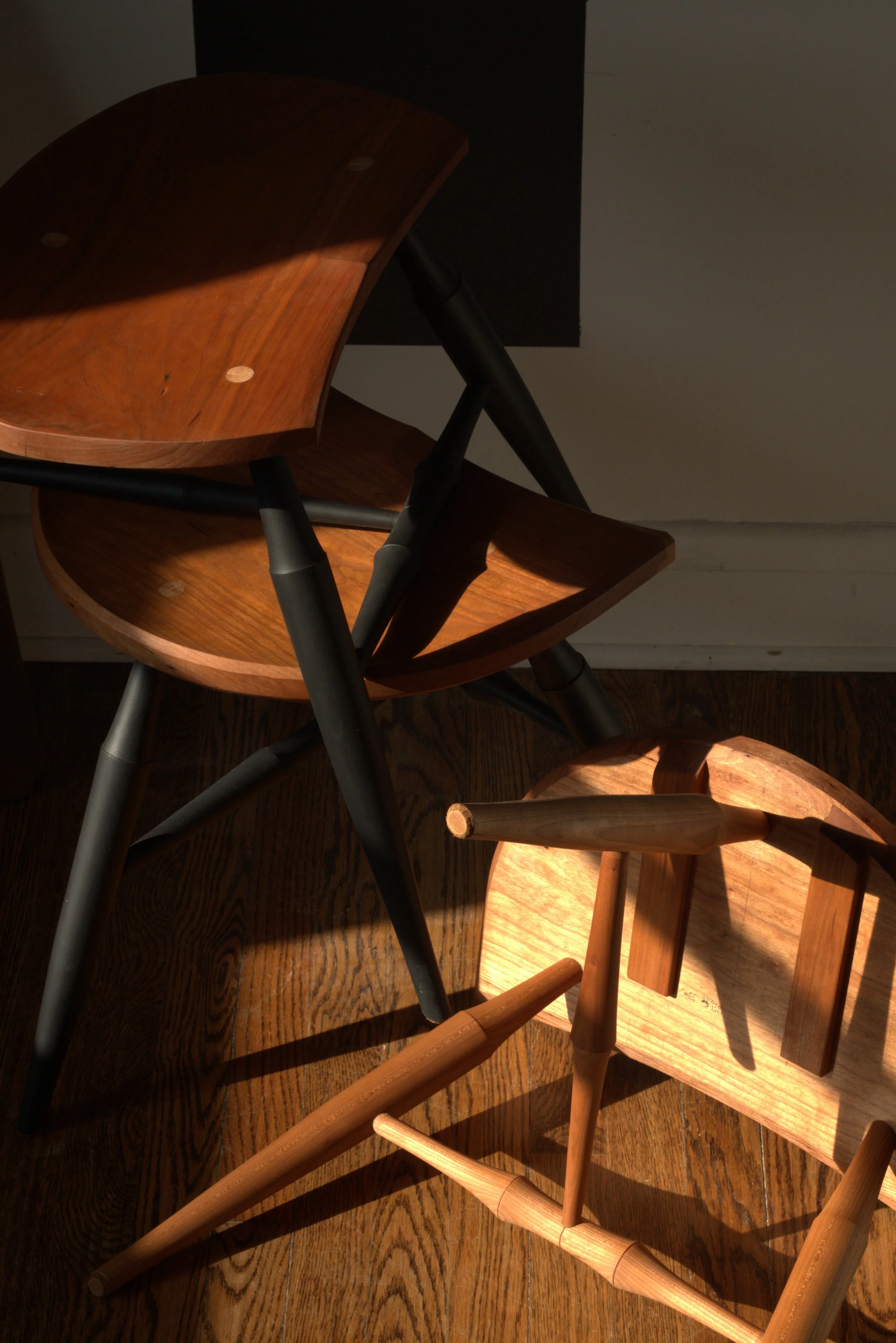 several wooden stools playfully arranged atop one another, all cast with golden-hour sunlight
