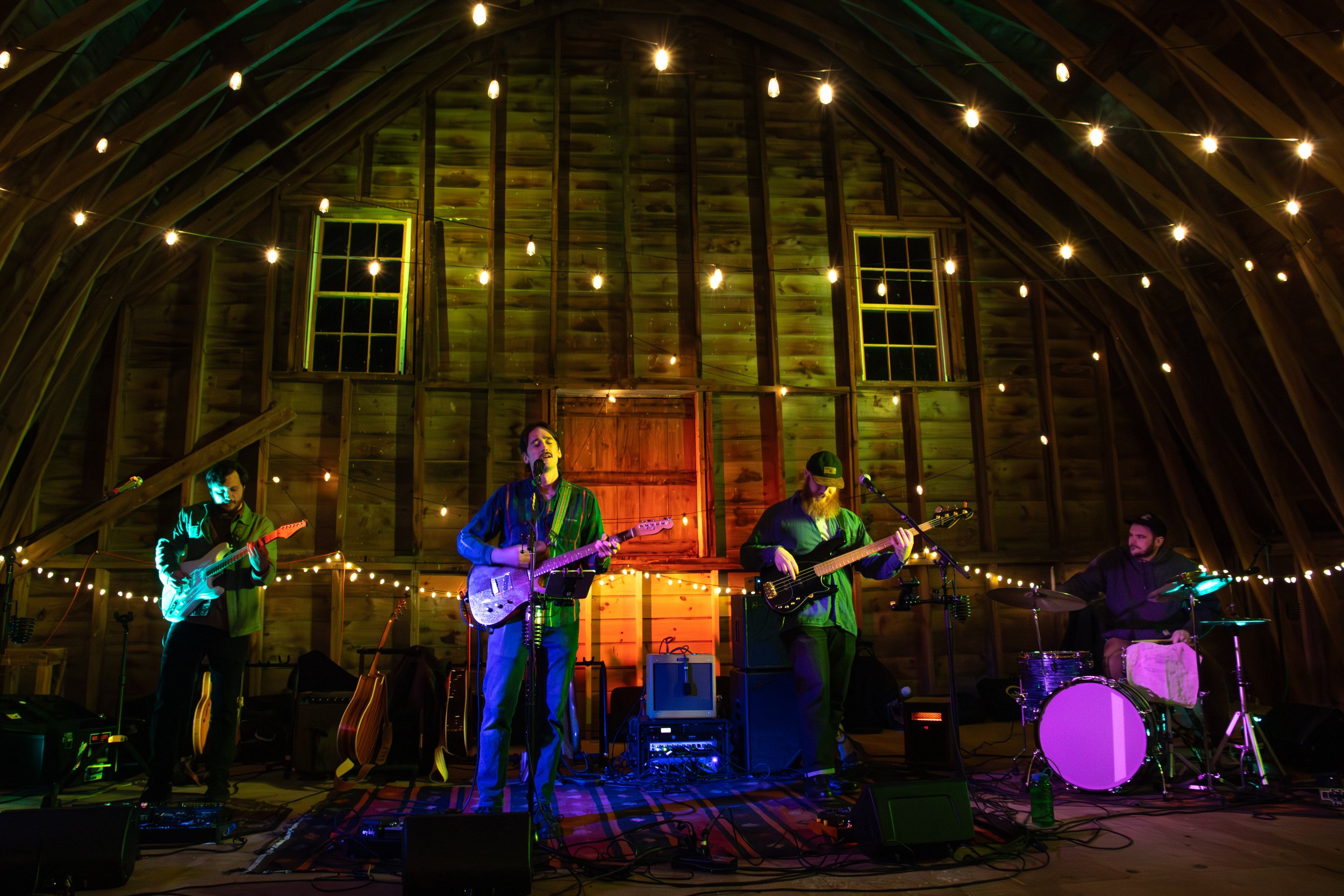 A live band performing in a rustic wooden barn decorated with string lights.