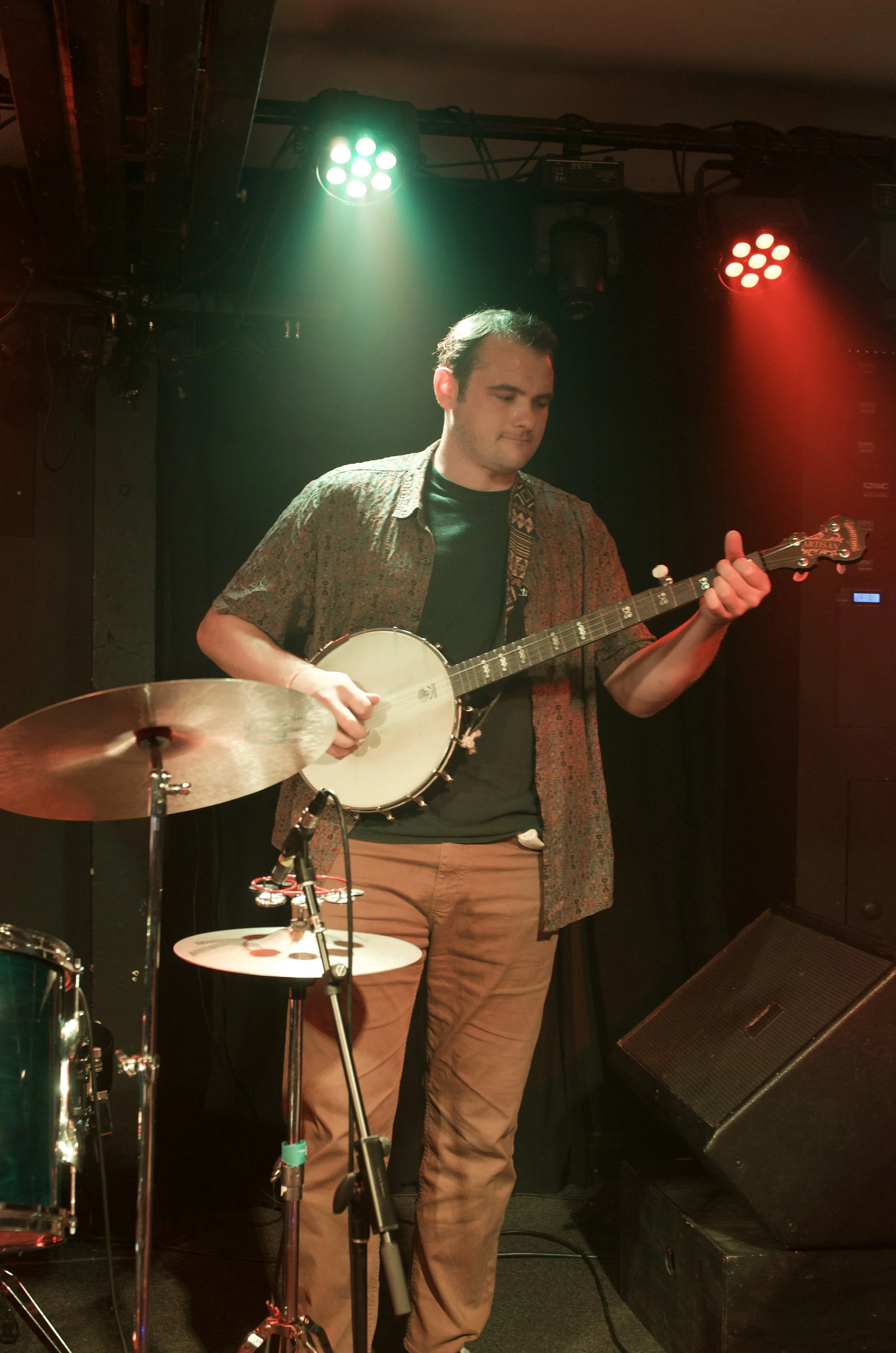 A man playing a banjo on stage with drums and stage lighting.