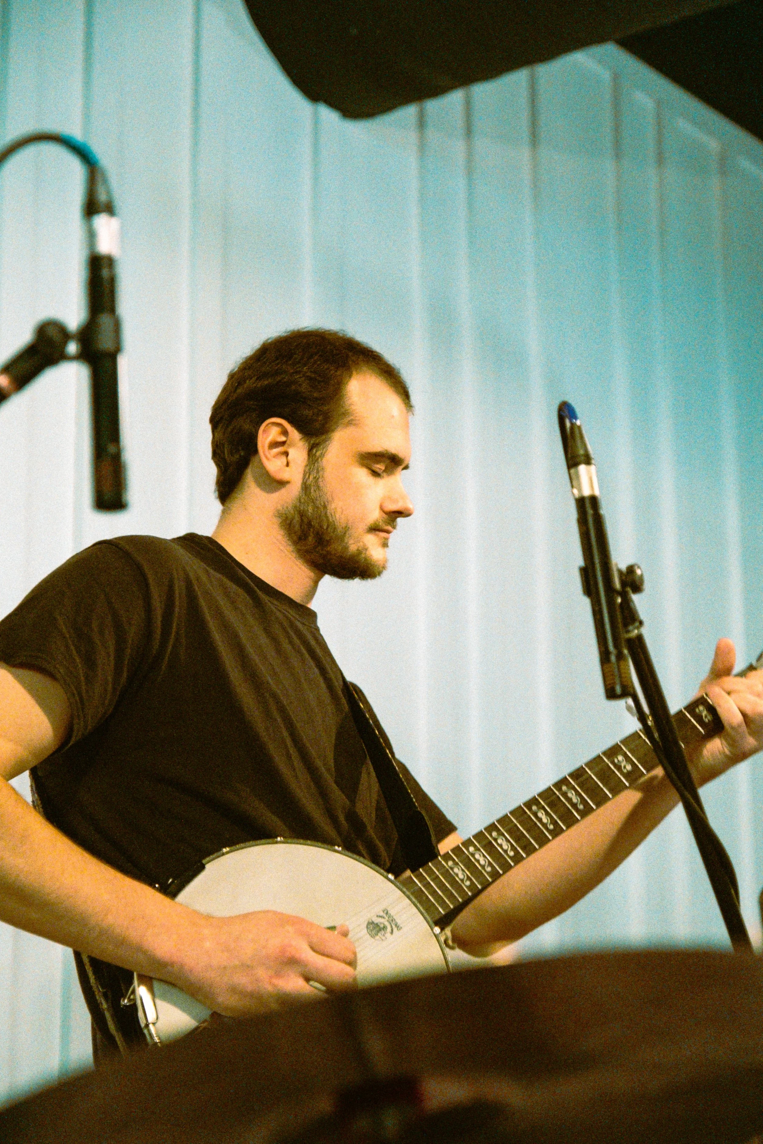 A man playing a banjo on stage, with a microphone nearby and a blue background.