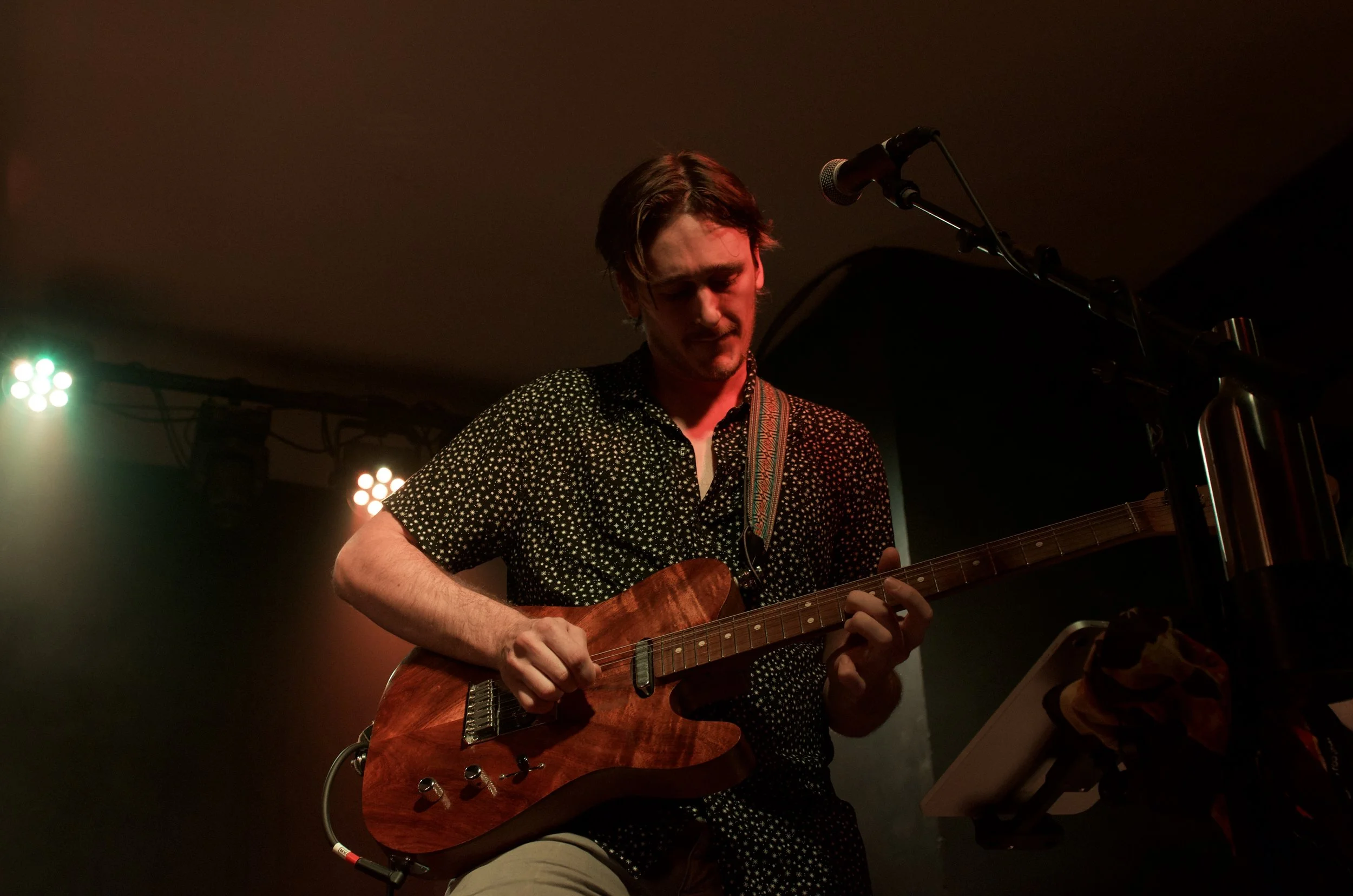 A young man playing an electric guitar on stage, with stage lights in the background.