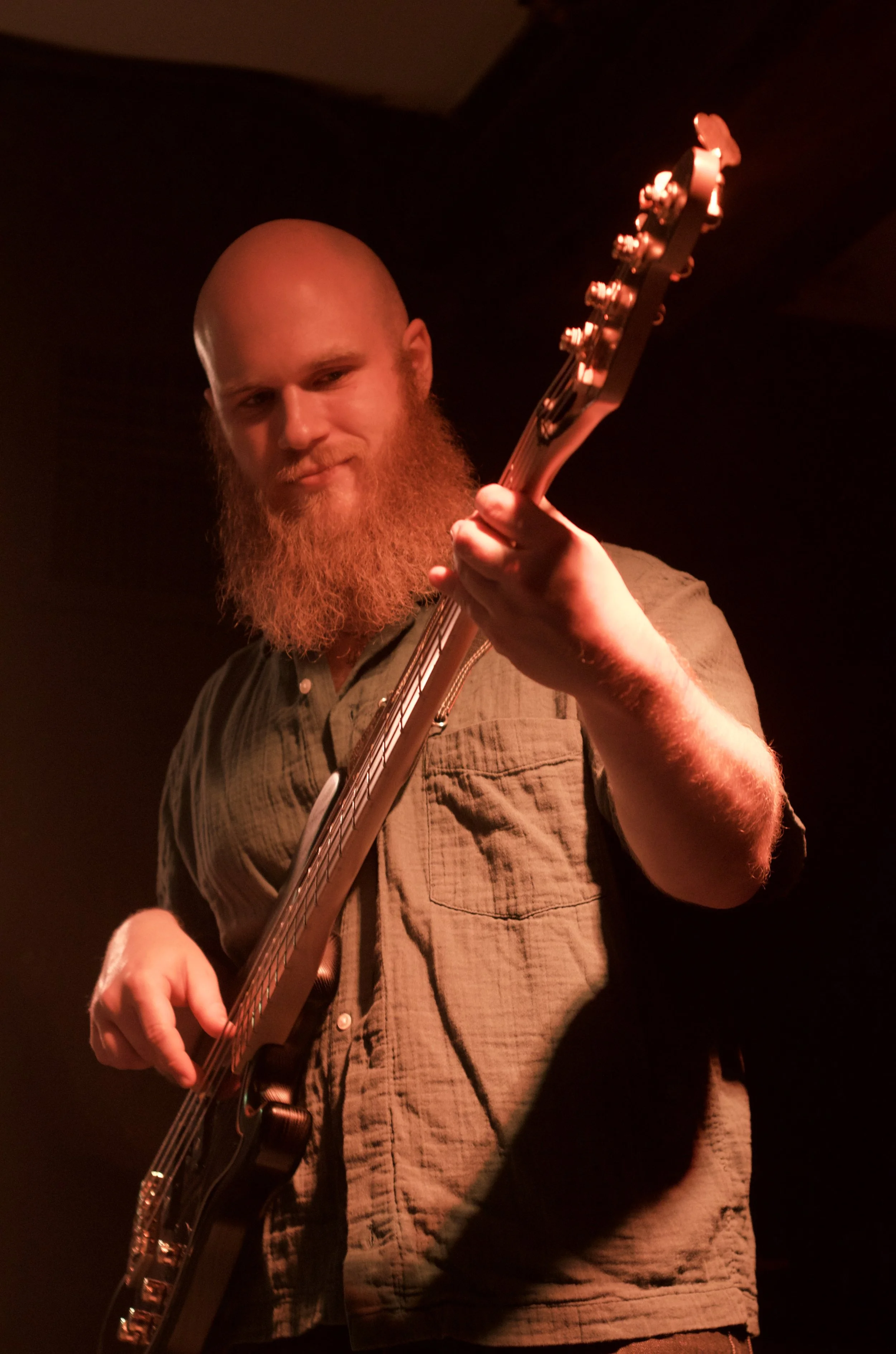 A bearded man playing an electric guitar on stage, illuminated by red lighting.