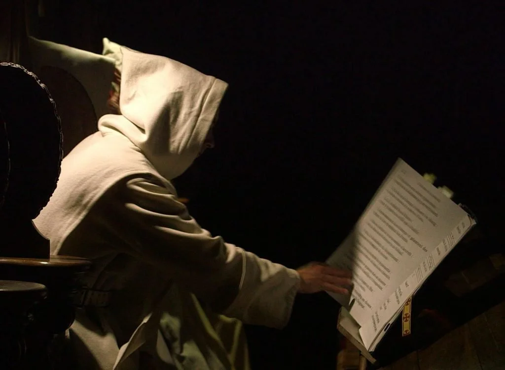A person wearing a hooded sweatshirt reading a book or menu in a dark setting.