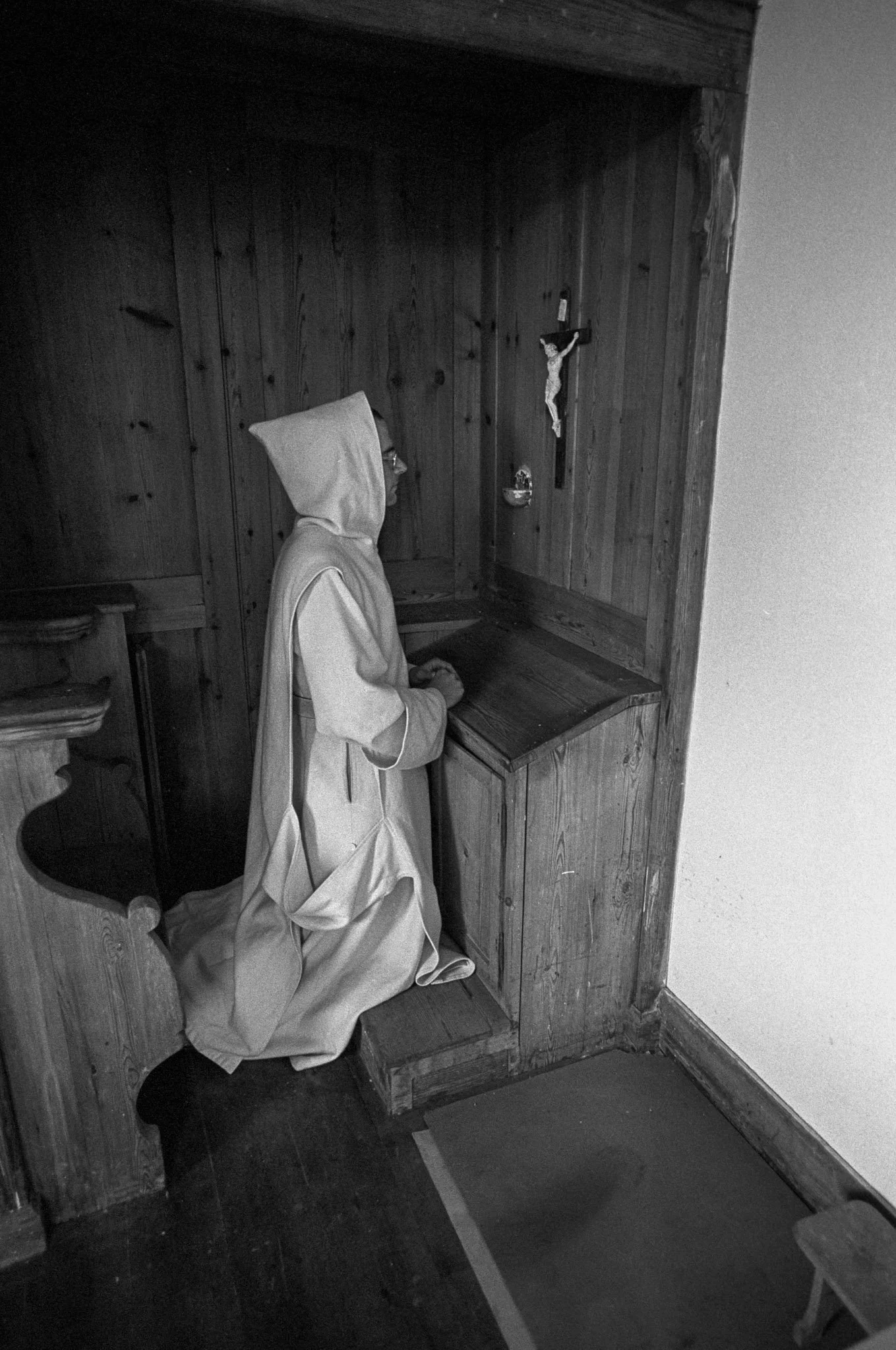 A statue of a person dressed as a nun kneeling in prayer in front of a small wooden altar with a crucifix.