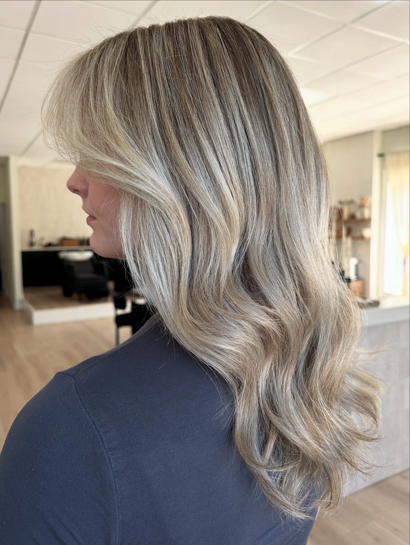 Side view of a woman with blonde, wavy, shoulder-length hair.