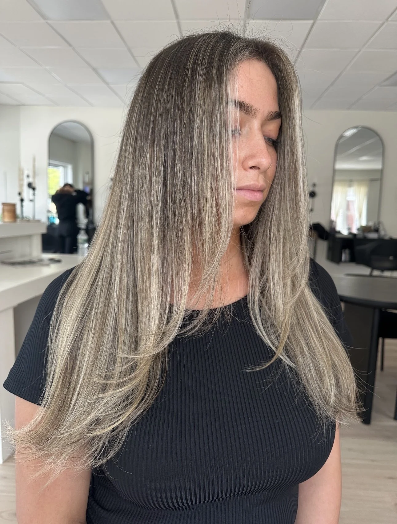 Woman with long, straight, highlighted hair in a salon setting.