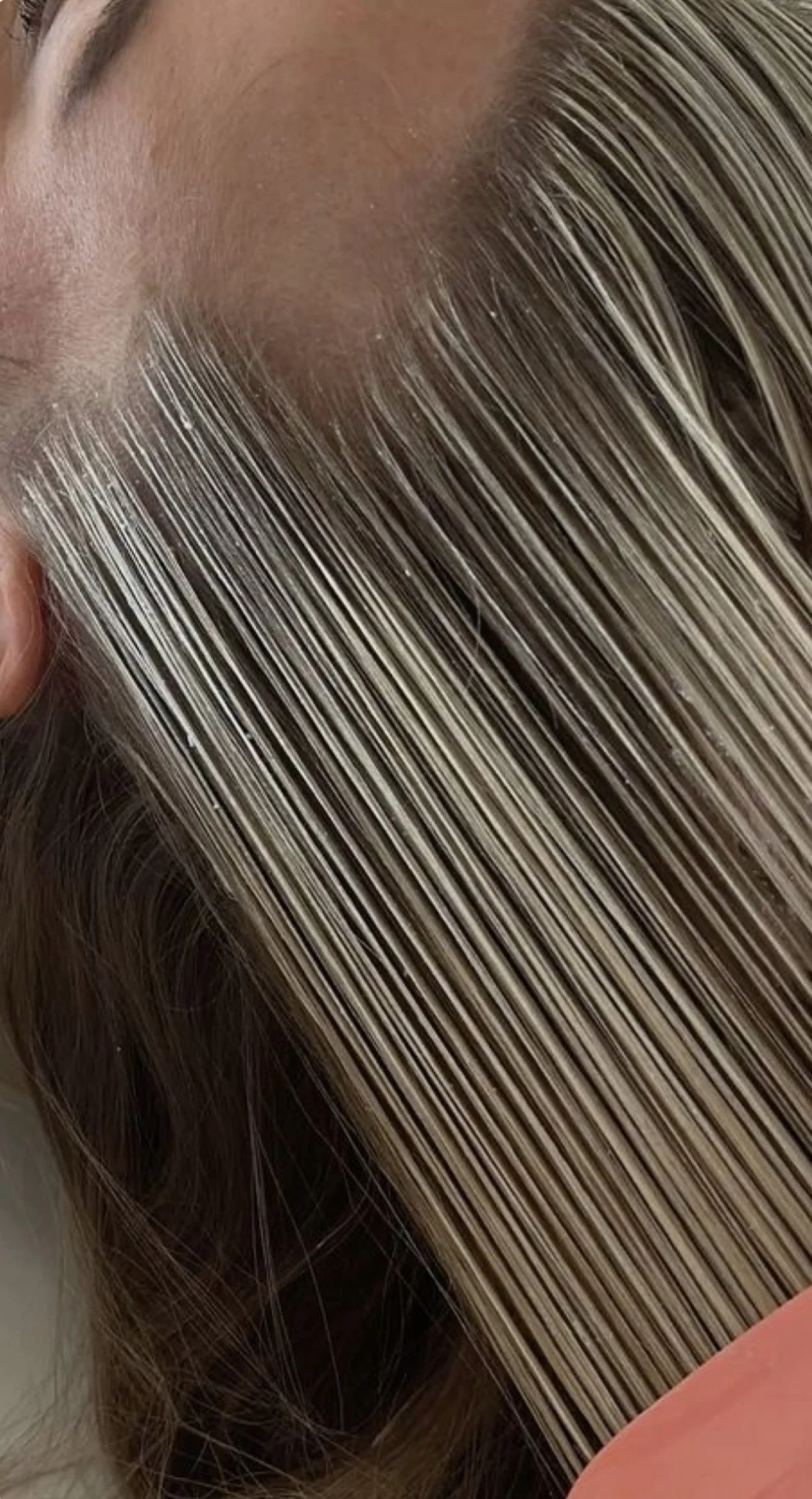 Close-up of a person's scalp showing shiny, blonde hair with highlights, and a finger holding a section of the hair.