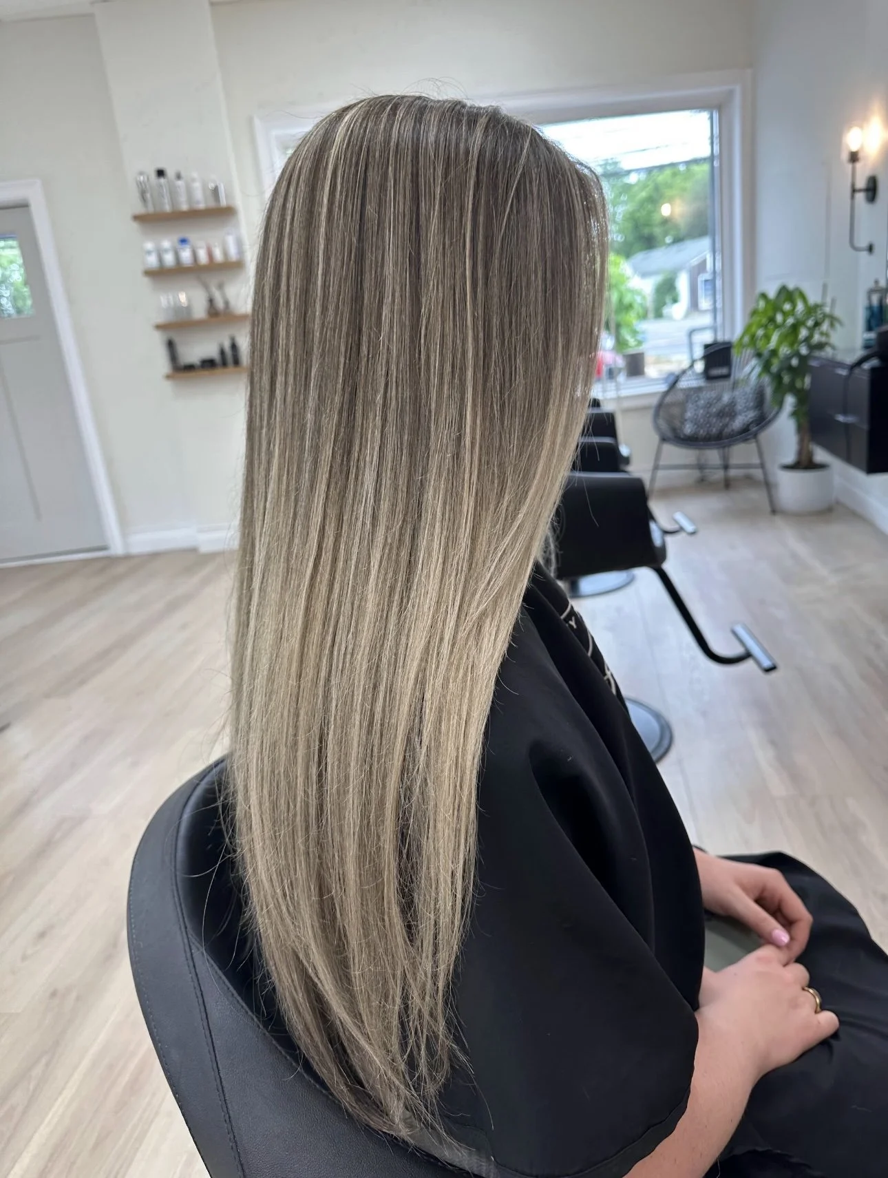 A woman with long, straight, blonde hair sitting in a salon chair inside a hair salon.