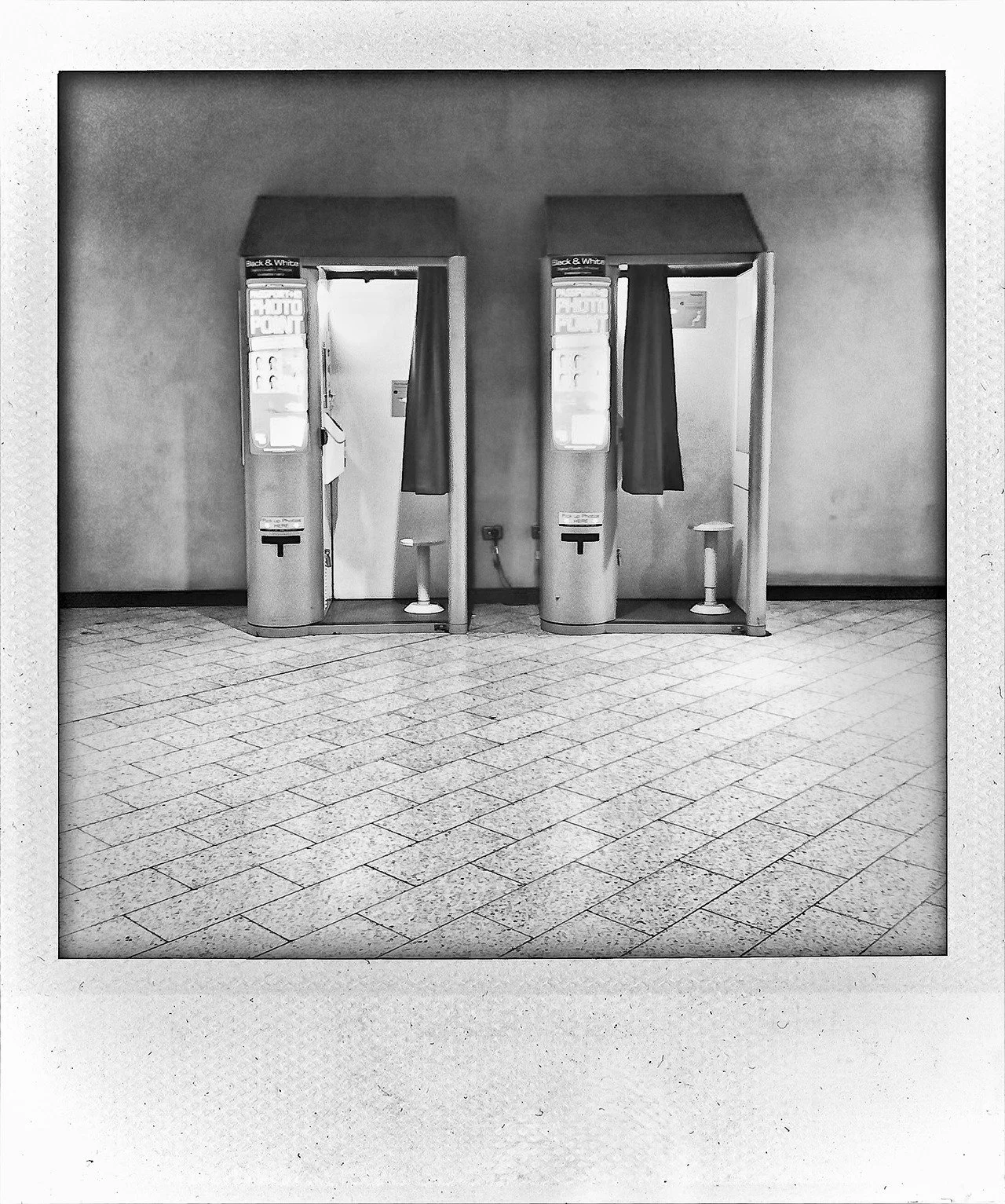 Two photo booth kiosks with curtains, located in an indoor space with tiled flooring.