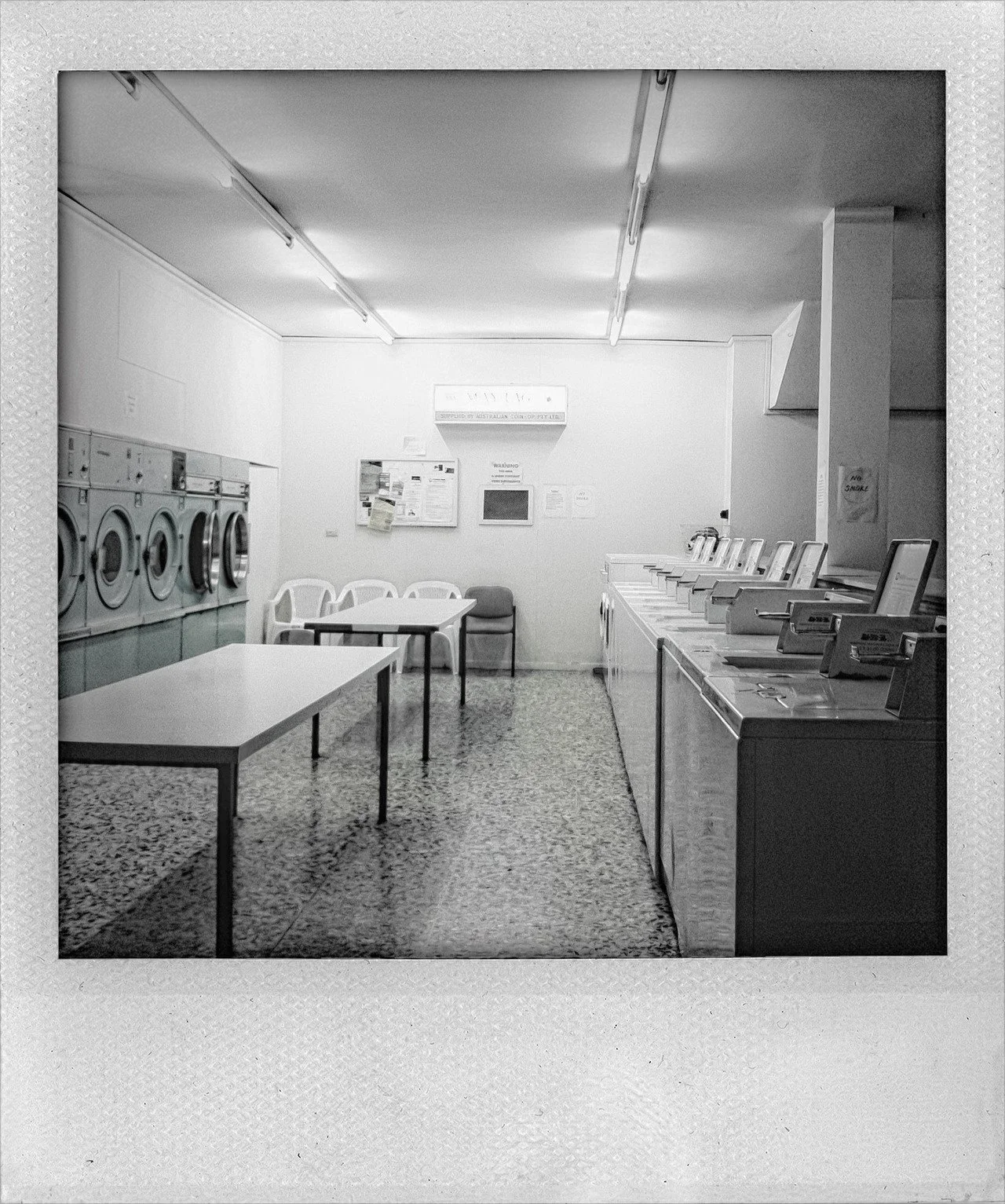 An empty laundry room with washing machines on the right, a table with chairs, and lockers on the left.