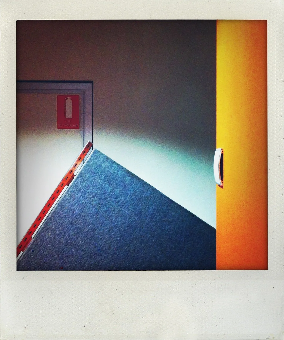 A wall with a red fire extinguisher sign, an orange wall, a diagonal blue panel, and a recessed handle on the orange wall.