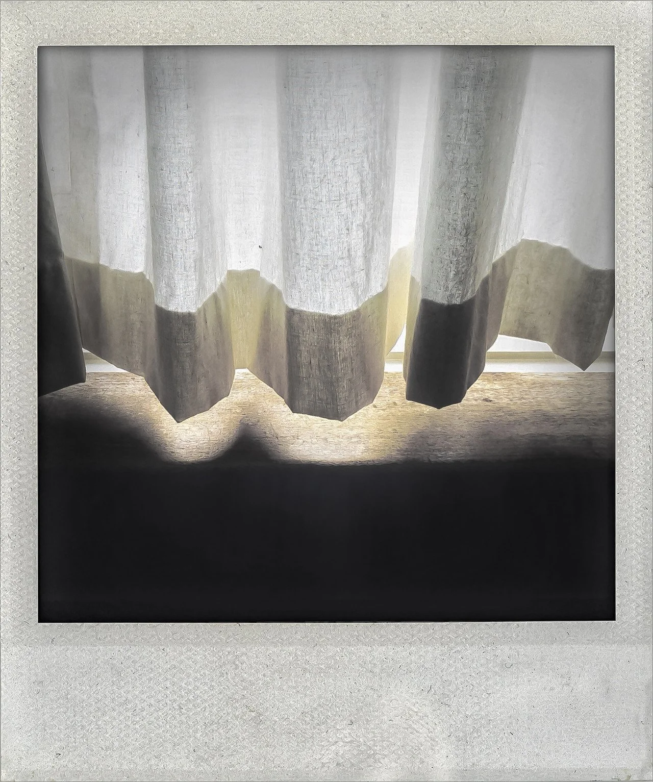 A window with sheer white curtains, letting light through. The curtains have a scalloped bottom edge, casting shadows on the surface below.