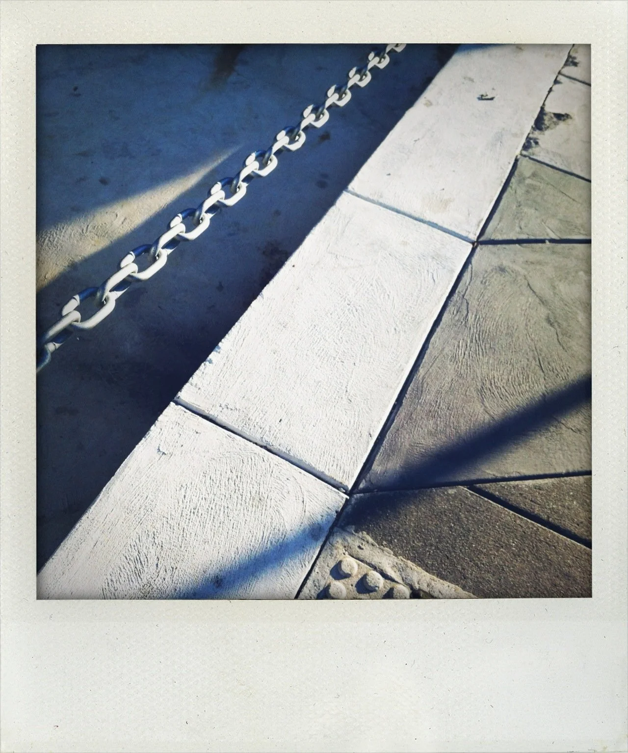 Close-up of a chain barrier and sidewalk tiles with shadows.