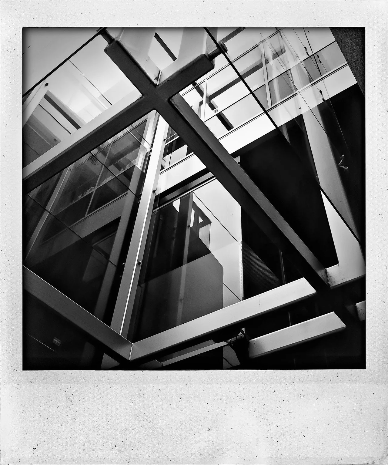 Black and white photo of modern glass and metal building structure, showing geometric lines and reflections.