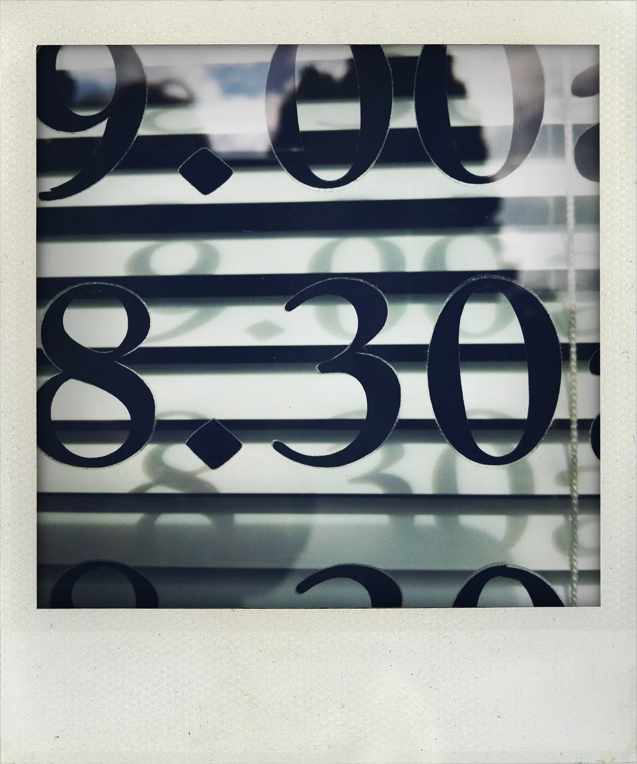 Close-up of a glass window with black numbers and a dot visible, showing the time as 8:30, with reflections and shadows in the background.