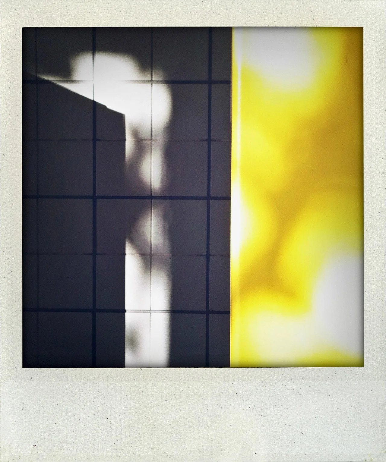 Shadow of a person on a tiled wall, with part of a yellow wall or poster on the right side.
