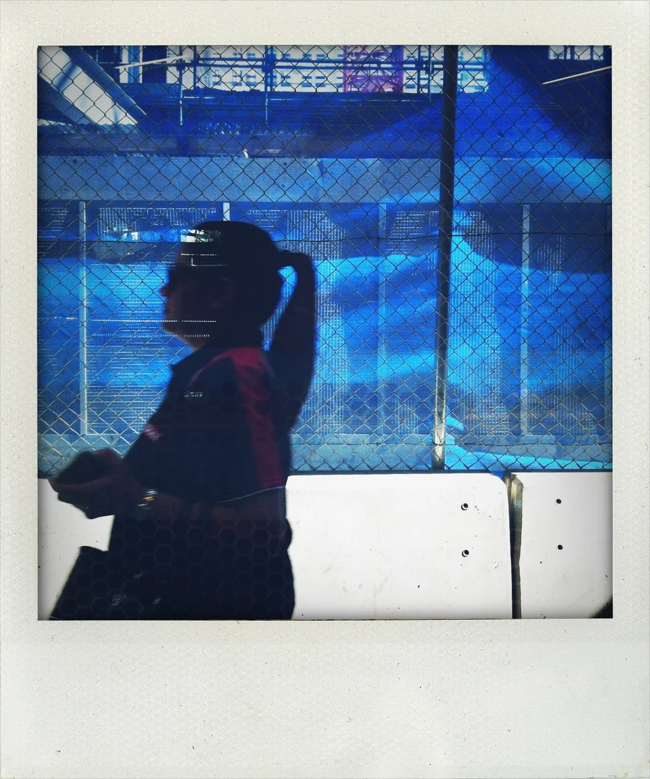 Silhouette of a woman walking past a fence with an illuminated blue background.