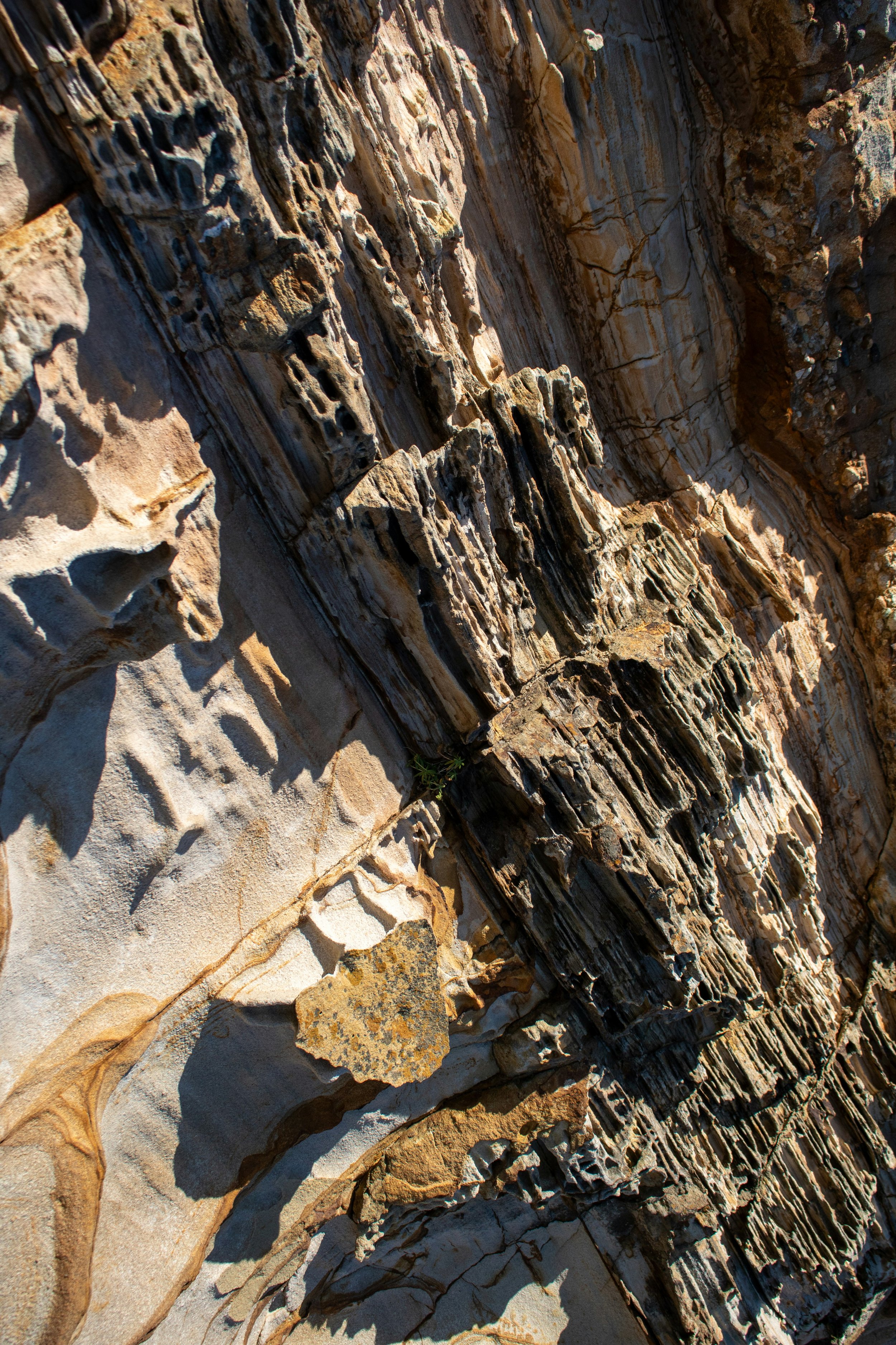 Close-up of layered, weathered rock formations with varying colors and textures, casting shadows in bright sunlight.