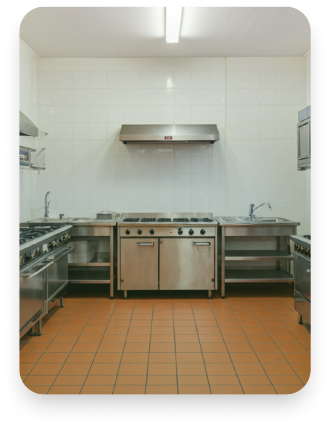 An empty commercial kitchen with stainless steel appliances, white tiled walls, and orange tiled flooring.