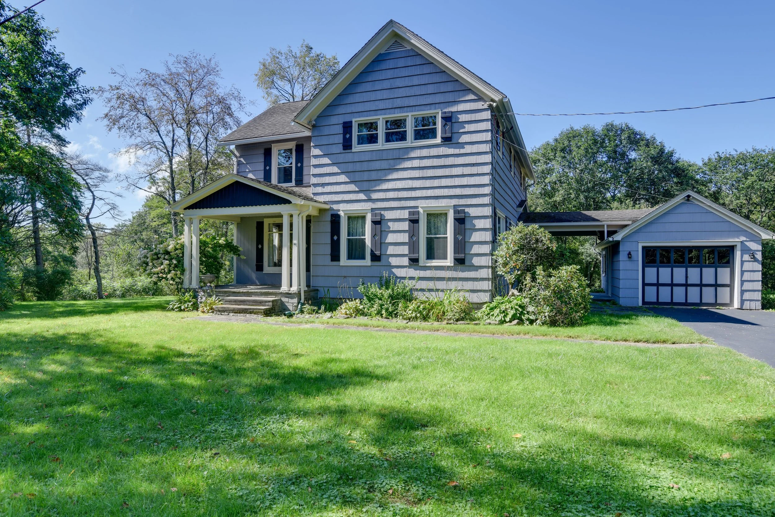 Blue two-story house with front porch, surrounded by green lawn and trees, with attached garage to the right.