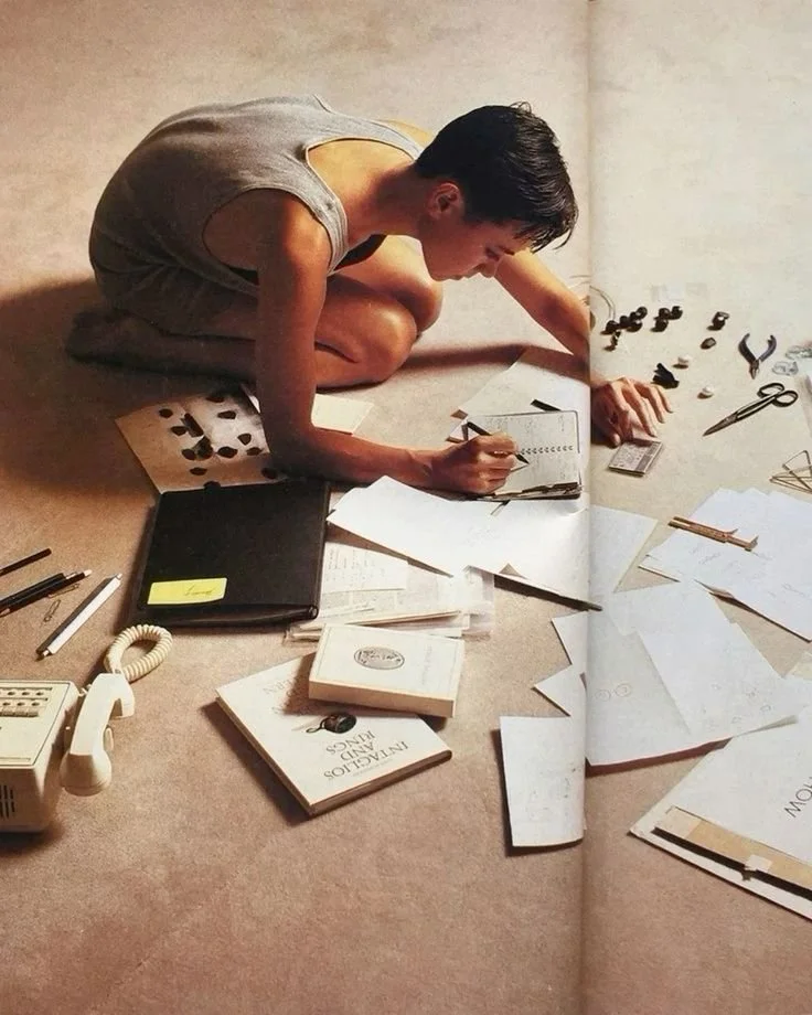 Person sitting on the floor, working with paper, scissors, and office supplies, surrounded by various documents and notebooks.