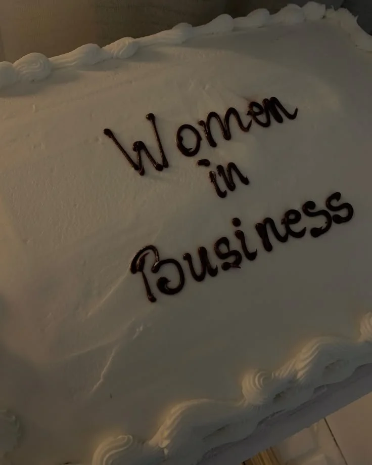 A white cake with decorative borders and the words 'Women in Business' written in chocolate on top.
